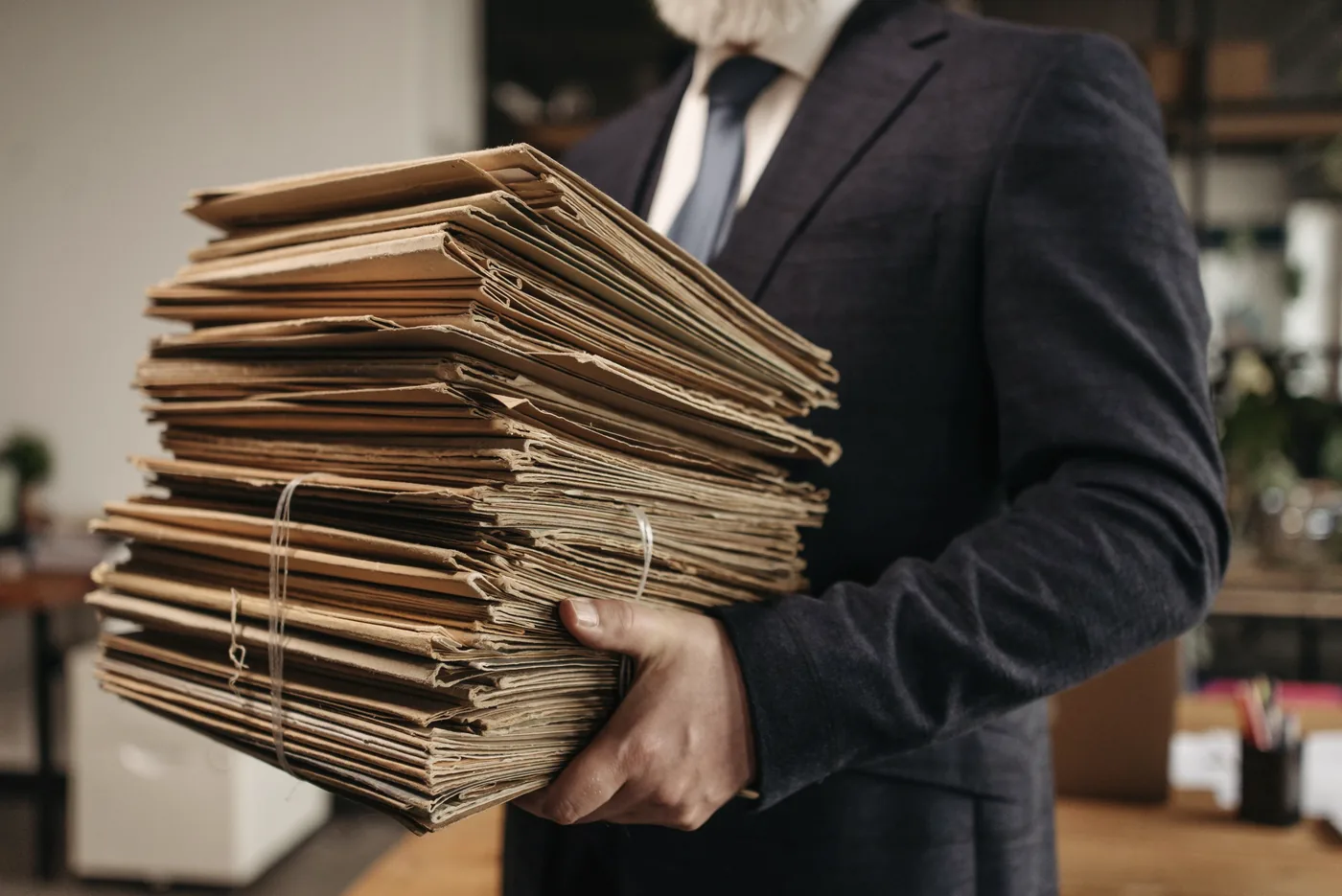 A lawyer in a suit carrying a tall stack of old paper case files