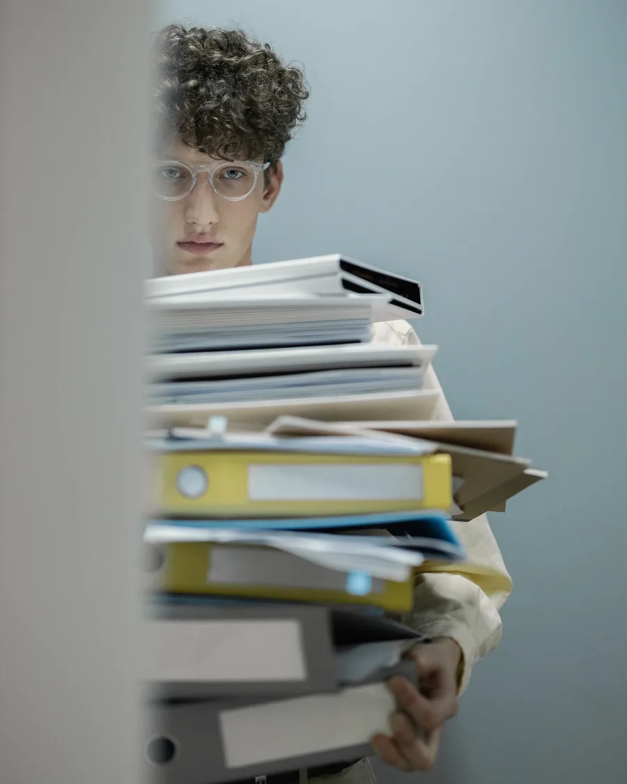 A clerk carrying a tall stack of binders and file folders