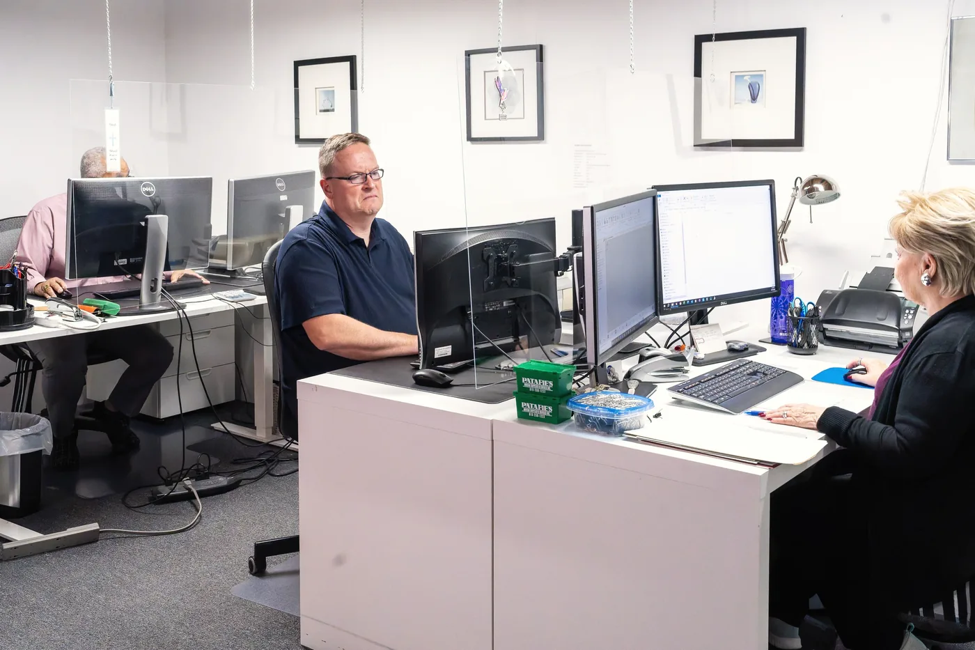 Jennifer et un collègue à leur bureau, avec Robert à un poste de travail derrière eux